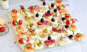 Variedad de canapés fríos fáciles y baratos: salmón, salami, jamón, queso, aceitunas, tomates cherry y más, perfectos para cualquier ocasión.