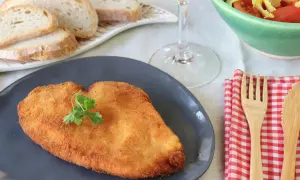 Un delicioso escalope de pollo dorado, servido con pan, ensalada y vino blanco.