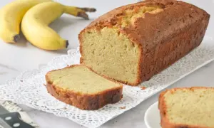 Un delicioso bizcocho de plátano recién horneado, con una rebanada cortada y dos plátanos amarillos al fondo.