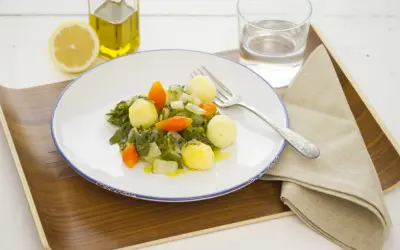 Plato de acelgas con patatas, zanahoria y cebolla, acompañado de limón, aceite de oliva y agua.