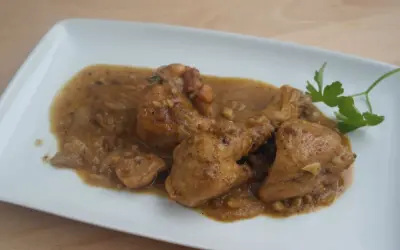 Sabroso pollo con almendras en una salsa dorada, servido en un plato blanco con una ramita de perejil.