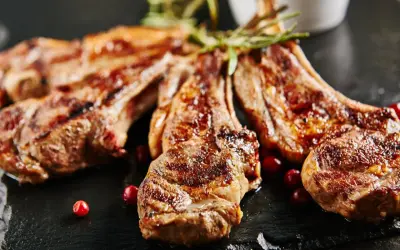 Chuletillas al sarmiento, jugosas y doradas, servidas con bayas rojas y romero sobre pizarra.