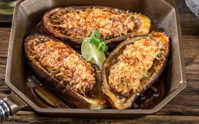 Berenjenas rellenas airfryer doradas y gratinadas, servidas en una sartén de hierro fundido con una rodaja de lima.