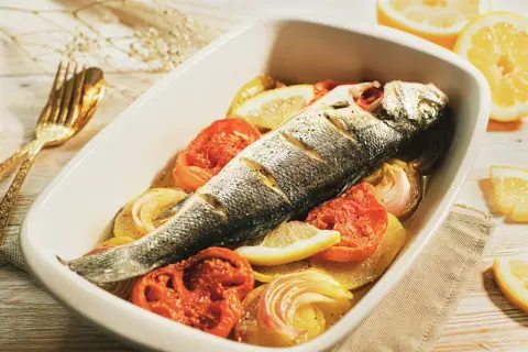 Lubina al horno con patatas, tomates y limón, lista para disfrutar.