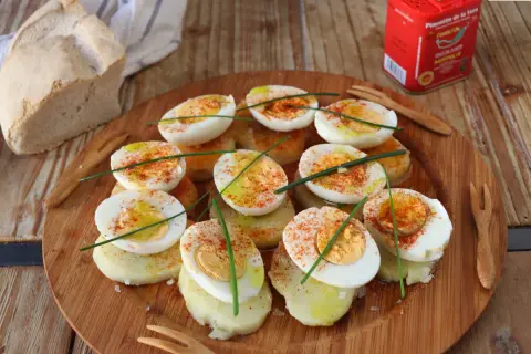 Deliciosos huevos a la gallega, cortados por la mitad y espolvoreados con pimentón, sobre rodajas de patata.