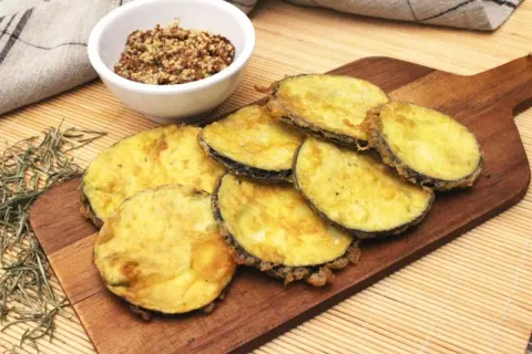 Berenjenas rebozadas con harina y huevo, doradas y crujientes, servidas en tabla de madera con un cuenco de mostaza.