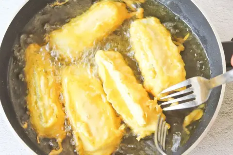 Soldaditos de pavia dorándose en aceite caliente. Un tenedor los voltea para una fritura perfecta.