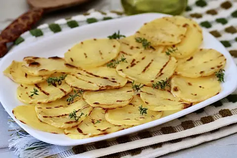 Deliciosas patatas a la plancha, finamente cortadas y con marcas de parrilla, adornadas con ramitas de tomillo fresco.