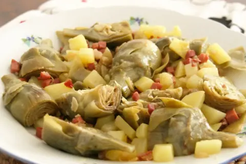 Plato de alcachofas tiernas y trocitos de patata, salpicado con dados de jamón serrano. Un bocado delicioso.