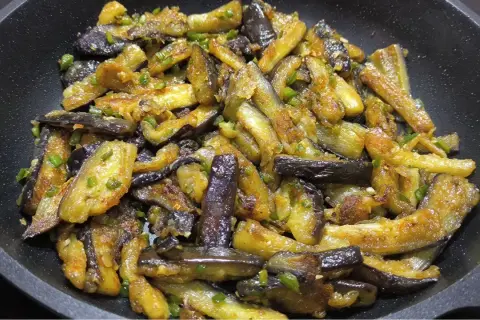 Berenjenas al ajillo salteadas en sartén, con trozos dorados y tiernos, salpicadas de ajo y perejil.