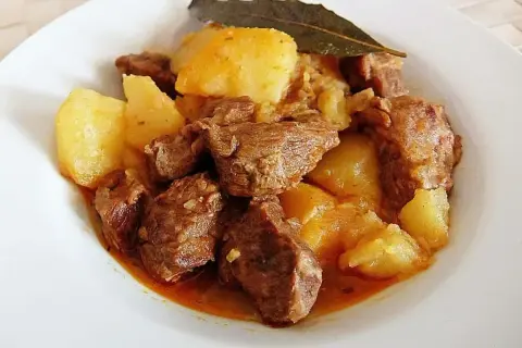 Plato de morcillo de ternera estofado con patatas y una hoja de laurel.