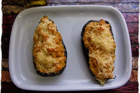 Dos berenjenas rellenas de gambas, gratinadas con queso, listas para disfrutar.