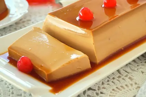 Un delicioso flan de café, con caramelo líquido y decorado con cerezas rojas, servido en un plato blanco.