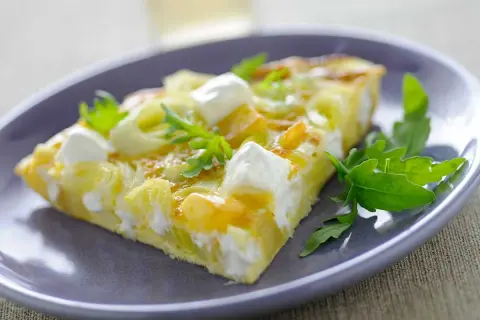 Porción de tortilla con puerros y queso de cabra, decorada con rúcula. Ideal para tus recetas con puerros.