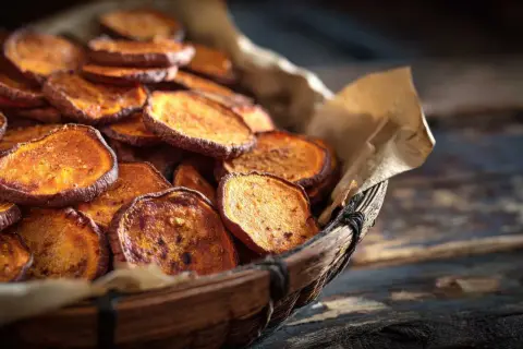 Rodajas de boniato al horno, crujientes y doradas, servidas en una cesta de mimbre.