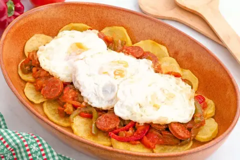 Huevos a la riojana servidos en una cazuela de barro, con patatas, chorizo y pimientos.