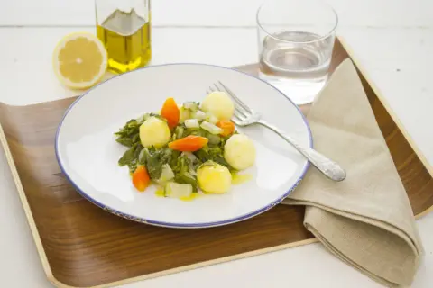 Plato de acelgas con patatas, zanahoria y cebolla, acompañado de limón, aceite de oliva y agua.