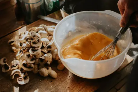 Un bol con huevos batidos y champiñones cortados en una tabla de madera, listos para un delicioso revuelto de setas.