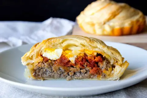 Porción de pastel de carne jugoso con huevo duro y salsa de tomate, envuelto en masa dorada.
