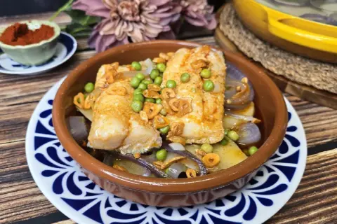 Bacalao a la gallega con patatas, guisantes y ajo frito en cazuela de barro. Un plato tradicional lleno de sabor.