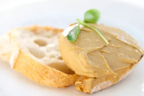 Tostada con paté de mejillones y una hoja verde como decoración.