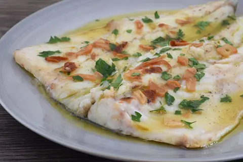 Lubina a la donostiarra, un plato de pescado blanco tierno bañado en aceite de oliva con láminas de ajo dorado y perejil fresco.
