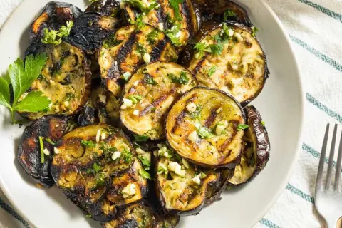 Rodajas de berenjena a la plancha, doradas y tiernas, con ajo picado y perejil fresco. Un plato delicioso y saludable.