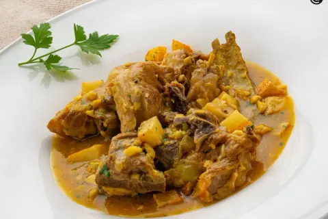Choto al ajillo, un guiso tierno de cabrito con patatas y un toque de ajo, servido en un plato blanco.