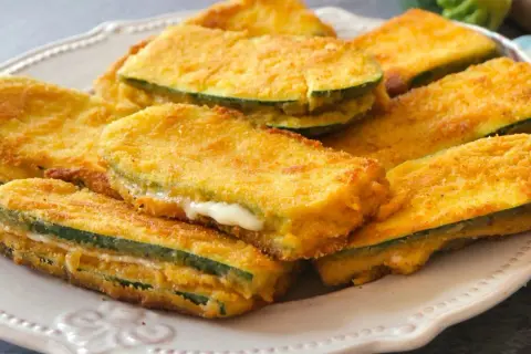 San jacobos de calabacín dorados y crujientes, rellenos de queso fundido, servidos en un plato blanco.