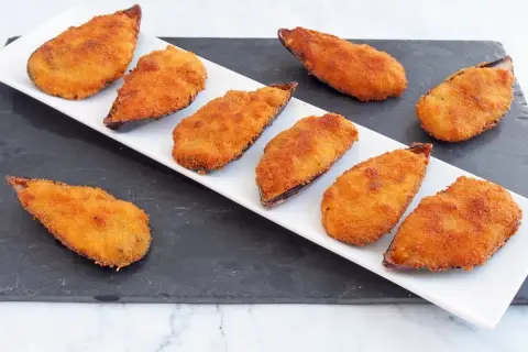 Mejillones tigre receta: mejillones rebozados y fritos, dorados y crujientes, servidos en una bandeja blanca sobre una pizarra.
