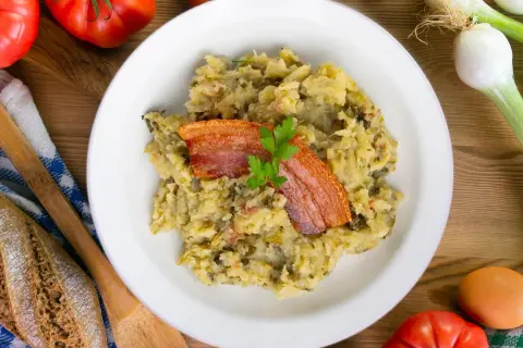Un plato de trinxat de montaña con crujiente panceta y perejil. Acompañado de pan rústico, tomates y cebolletas.
