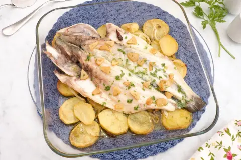 Lubina al horno con patatas y ajo, recién salida del horno, lista para servir.