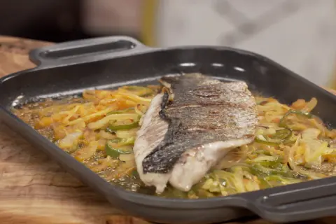 Filete de corvina a la roteña, con verduras salteadas en una sartén de hierro fundido.