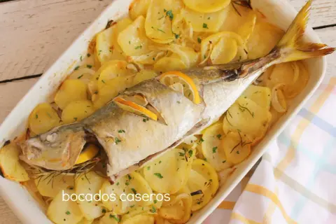 Un delicioso chicharro al horno con patatas, limón y romero, listo para servir.
