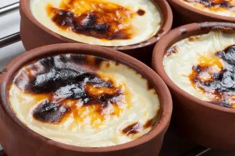 Cuatro cazuelas de barro con tarta de arroz horneada, con una capa superior dorada y caramelizada.