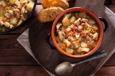 Un reconfortante guiso de pollo con patatas de la abuela, servido en cazuela de barro con pan tostado.