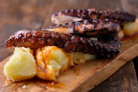 Pulpo tierno con patatas y pimentón, servido en tabla de madera.