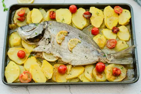Delicioso sargo al horno con patatas y tomates cherry, listo para servir.