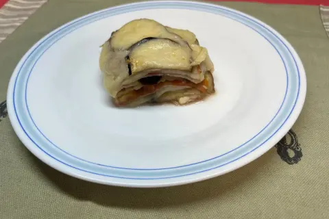 Un delicioso pastel de berenjenas gratinado con queso, servido en un plato blanco con borde azul.