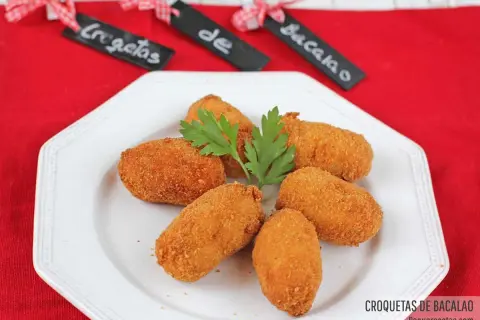 Croquetas de bacalao doradas y crujientes, servidas en un plato blanco con perejil.