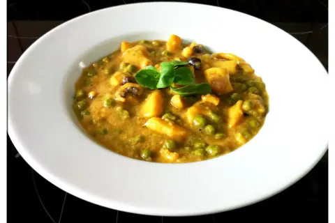 Plato de jibia en salsa de almendras, con guisantes y trozos de patata, decorado con una hoja verde.
