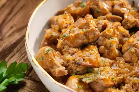 Un delicioso plato de caldereta de cordero, con trozos tiernos de carne en una salsa dorada y aromática, adornado con perejil fresco.