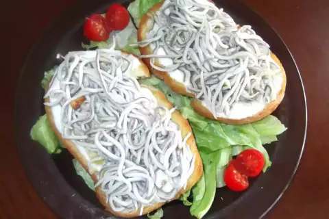 Dos tostas de gulas sobre lechuga y tomate cherry, un bocado delicioso.