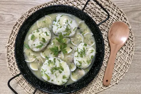 Merluza a la vasca, un plato tradicional con trozos de pescado blanco en una salsa cremosa con almejas y perejil picado.