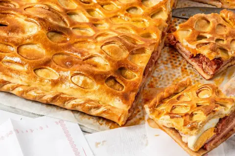 Un delicioso hornazo de Salamanca, con su masa dorada y relleno de carne y huevo duro, listo para ser disfrutado.