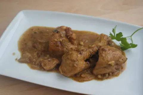 Sabroso pollo con almendras en una salsa dorada, servido en un plato blanco con una ramita de perejil.