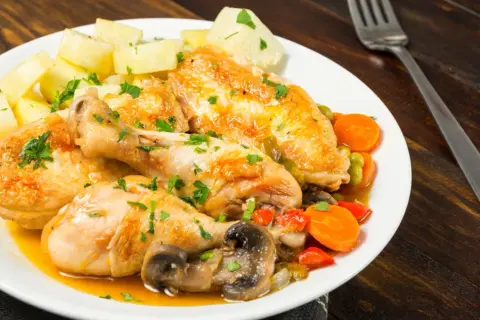 Sabroso pollo a la pepitoria con patatas, zanahorias, guisantes y champiñones, todo espolvoreado con perejil fresco.