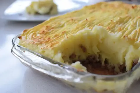 Un delicioso pastel de papa recién horneado, con una capa dorada y texturizada de puré de papa sobre un relleno jugoso.