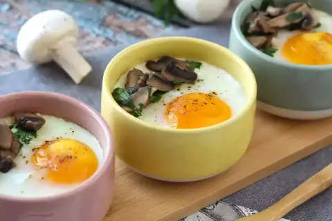 Deliciosos huevos al horno con champiñones y perejil, servidos en coloridas tazas. Un desayuno perfecto.