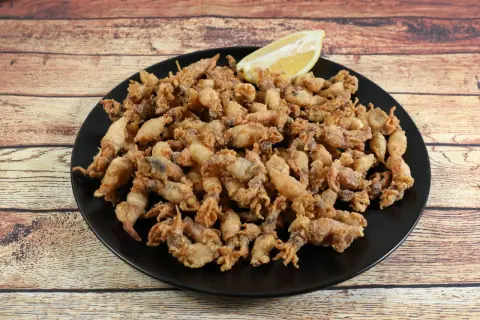 Un plato negro rebosante de puntillas de calamar crujientes, con un gajo de limón esperando para dar el toque final.